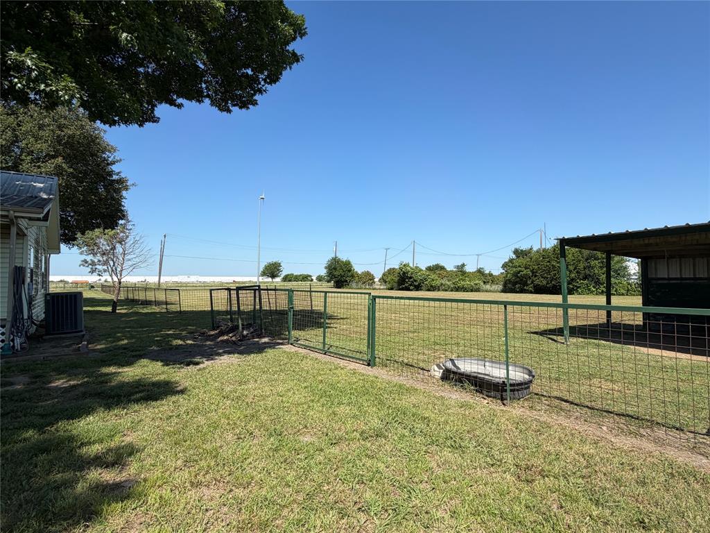330 South Goode Road Wilmer, TX 75172 - Photo 31 of 37 Expansive grassy area with a partial metal fence and a utility structure featuring a metal roof
