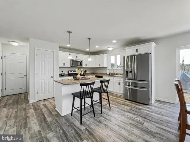 a kitchen with stainless steel appliances a refrigerator a stove top oven a sink dishwasher and white cabinets with wooden floor