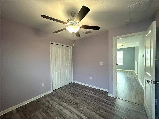 an empty room with wooden floor fan and windows