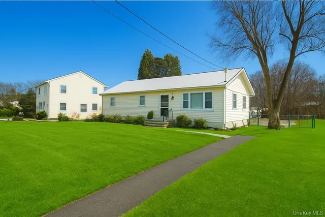 a view of a white house in front of a big yard with large trees