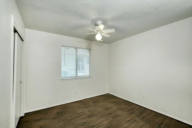 an empty room with wooden floor ceiling fan and windows