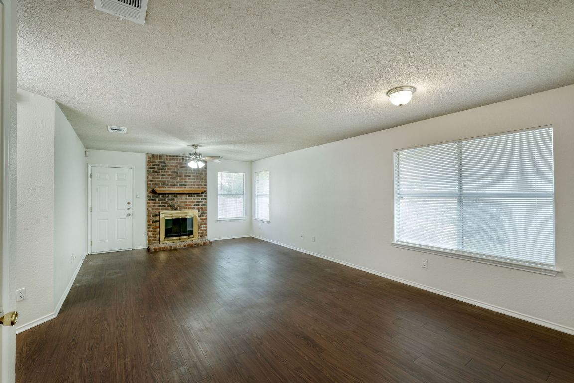 1304 Garden Path Cove Round Rock, TX 78664 - Photo 2 of 14 Unfurnished living room featuring dark wood-style flooring, a textured ceiling, a brick fireplace, and a ceiling fan