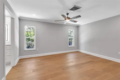 an empty room with wooden floor a ceiling fan and windows