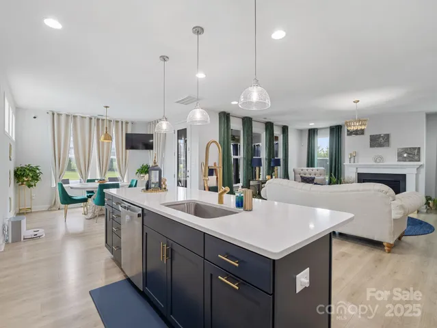 a large white kitchen with a large island oven a sink dishwasher and a fireplace with wooden floor
