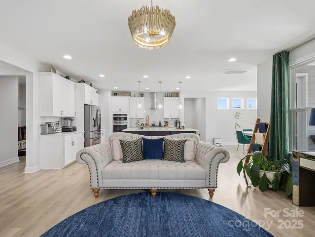 a living room with white couches and kitchen view with wooden floor