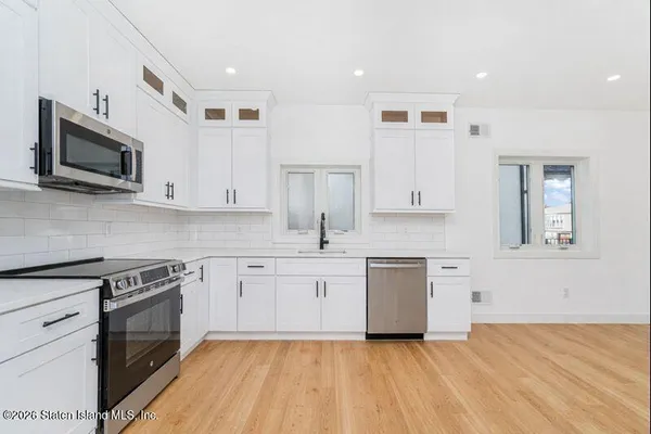 a kitchen with stainless steel appliances granite countertop a stove top oven a sink dishwasher and white cabinets with wooden floor