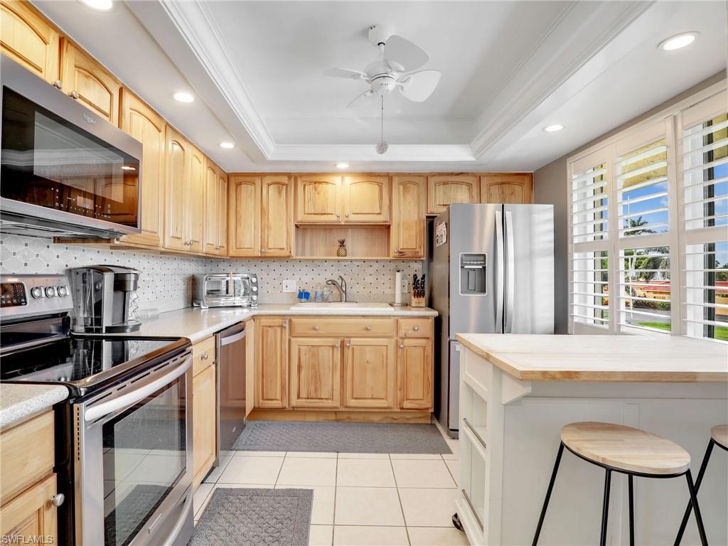 119 Harrison Road, Unit 16 Naples, FL 34112 - Photo 3 of 26 Kitchen with stainless steel appliances, open shelves, a tray ceiling, ceiling fan, and decorative backsplash