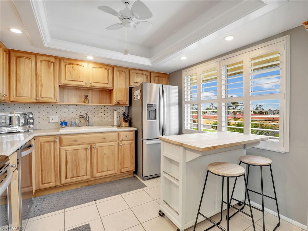 119 Harrison Road, Unit 16 Naples, FL 34112 - Photo 5 of 26 Kitchen with stainless steel appliances, open shelves, a tray ceiling, light countertops, and backsplash