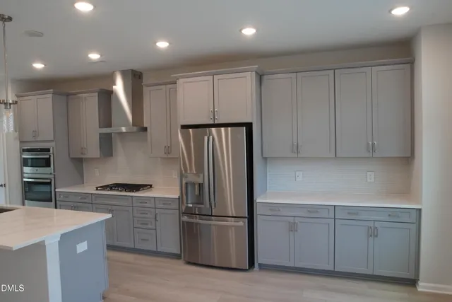 a kitchen with stainless steel appliances granite countertop a refrigerator a sink dishwasher a stove and white countertops with wooden floor