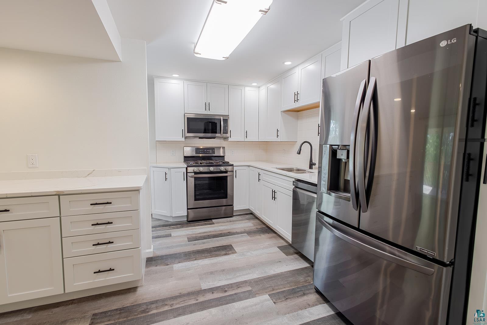 29 Ridge Road Esko, MN 55733 - Photo 11 of 41 Modern kitchen featuring white shaker cabinetry, stainless steel appliances, light-toned countertops, a matte black faucet, and wood-finish flooring