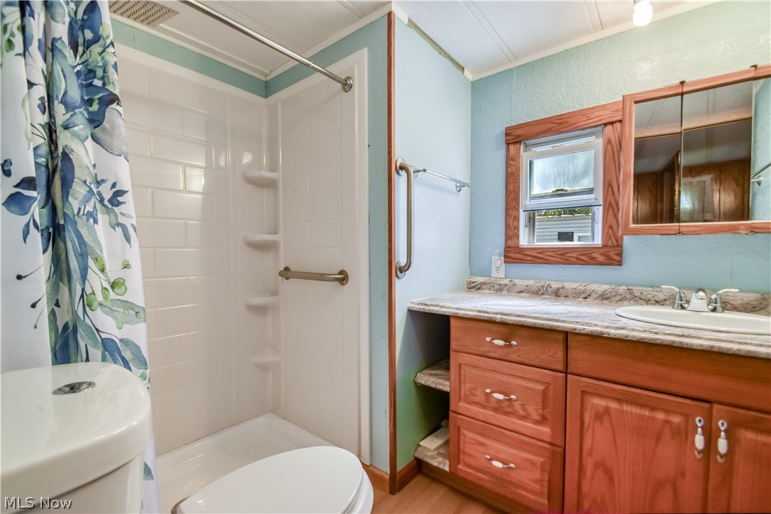 112 Lakeside Way Southwest Warren, OH 44481 - Photo 10 of 16 Bathroom featuring a shower with built-in shelving and grab bars, a single vanity with a stone-finish countertop, and a wood-framed window