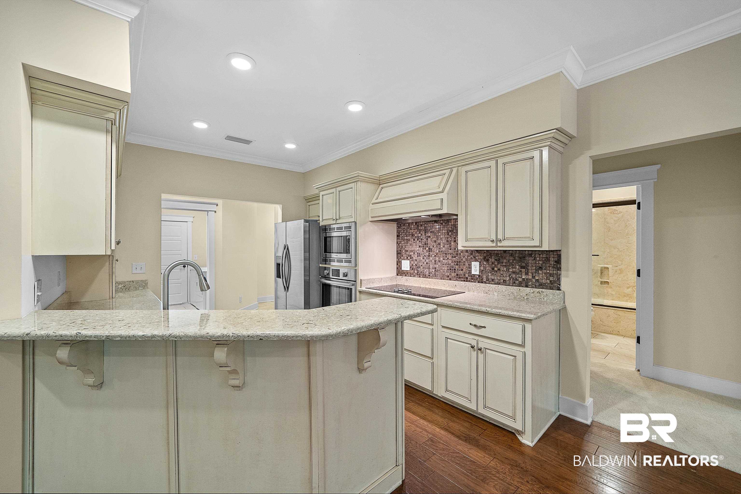 356 Liberty Street Fairhope, AL 36532 - Photo 7 of 39 Kitchen featuring light stone countertops, a breakfast bar area, crown molding, dark wood-type flooring, and a peninsula