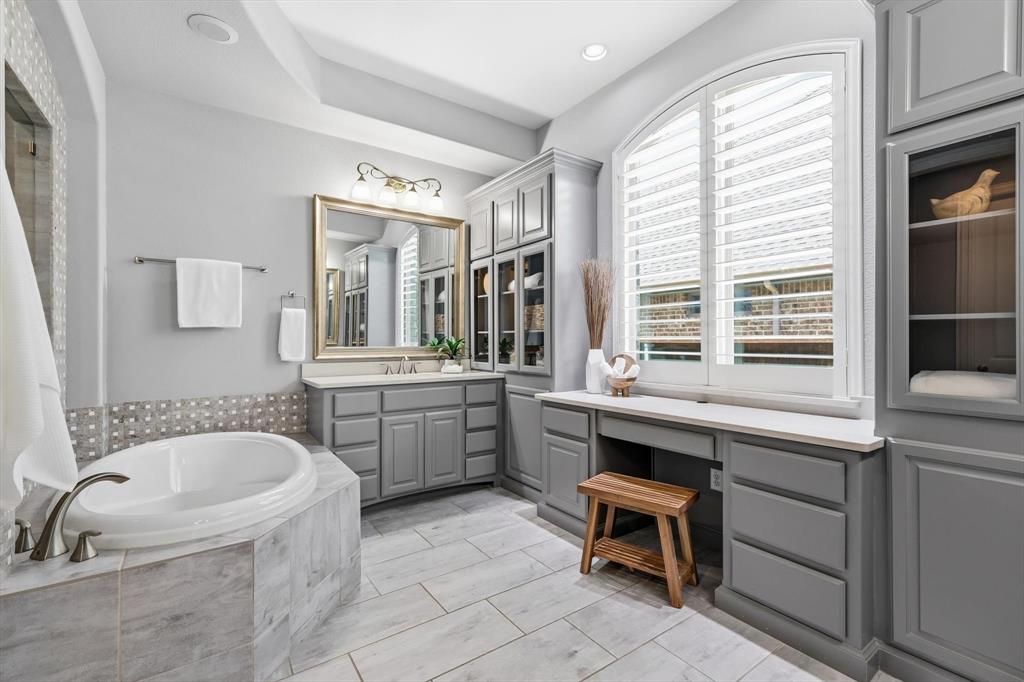 1933 Snapdragon Road Frisco, TX 75033 - Photo 20 of 40 Bathroom featuring a built-in soaking tub with marble-finish surround, extensive cabinetry, dual vanity with undermount sink, and arched window with plantation shutters