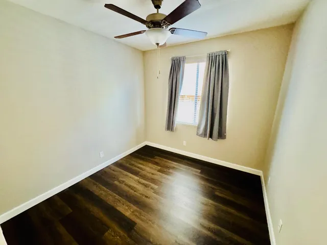 an empty room with wooden floor fan and windows