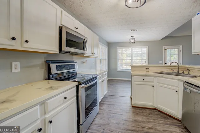 a kitchen with stainless steel appliances granite countertop a stove top oven a sink dishwasher and a microwave oven with white cabinets