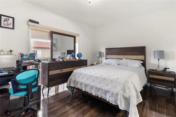 a bedroom with a bed a desk and chair with wooden floor