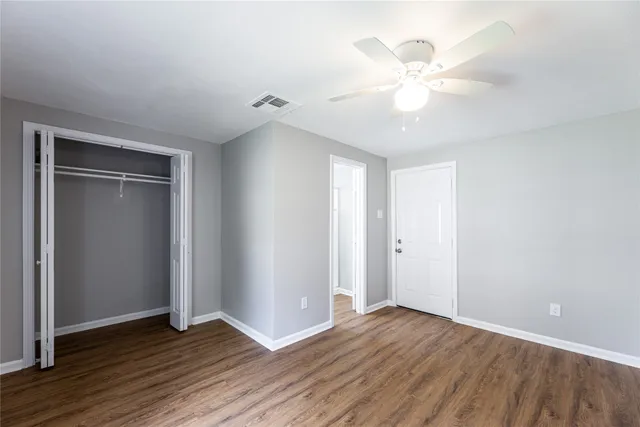 an empty room with wooden floor fan and windows