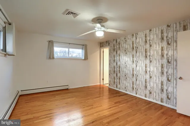 a view of an empty room with wooden floor and a ceiling fan