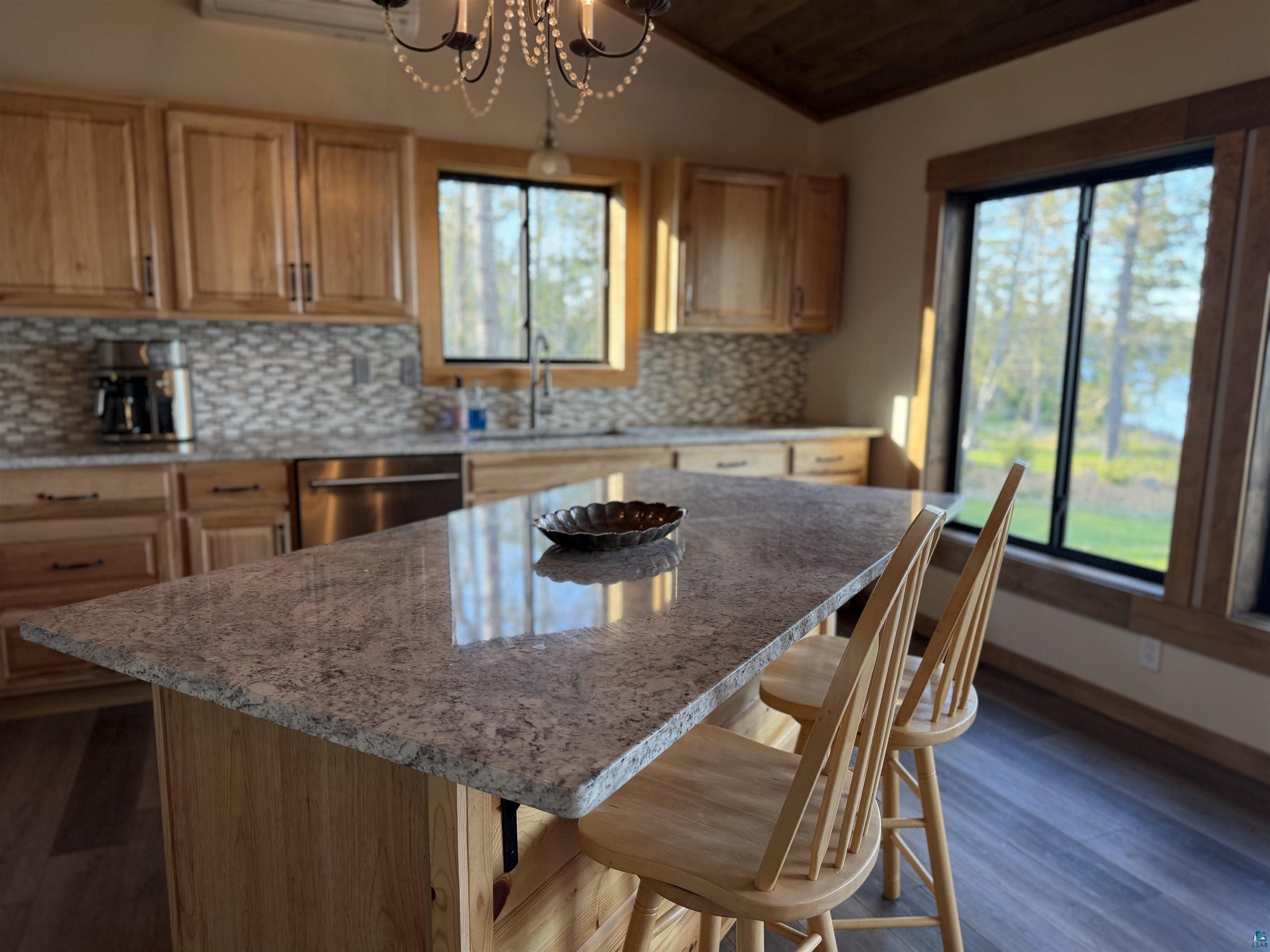 5274 Marble Lake Road Two Harbors, MN 55616 - Photo 19 of 79 Kitchen island featuring a light-toned stone countertop, wood-finish cabinetry, a decorative backsplash, and stainless-steel appliances
