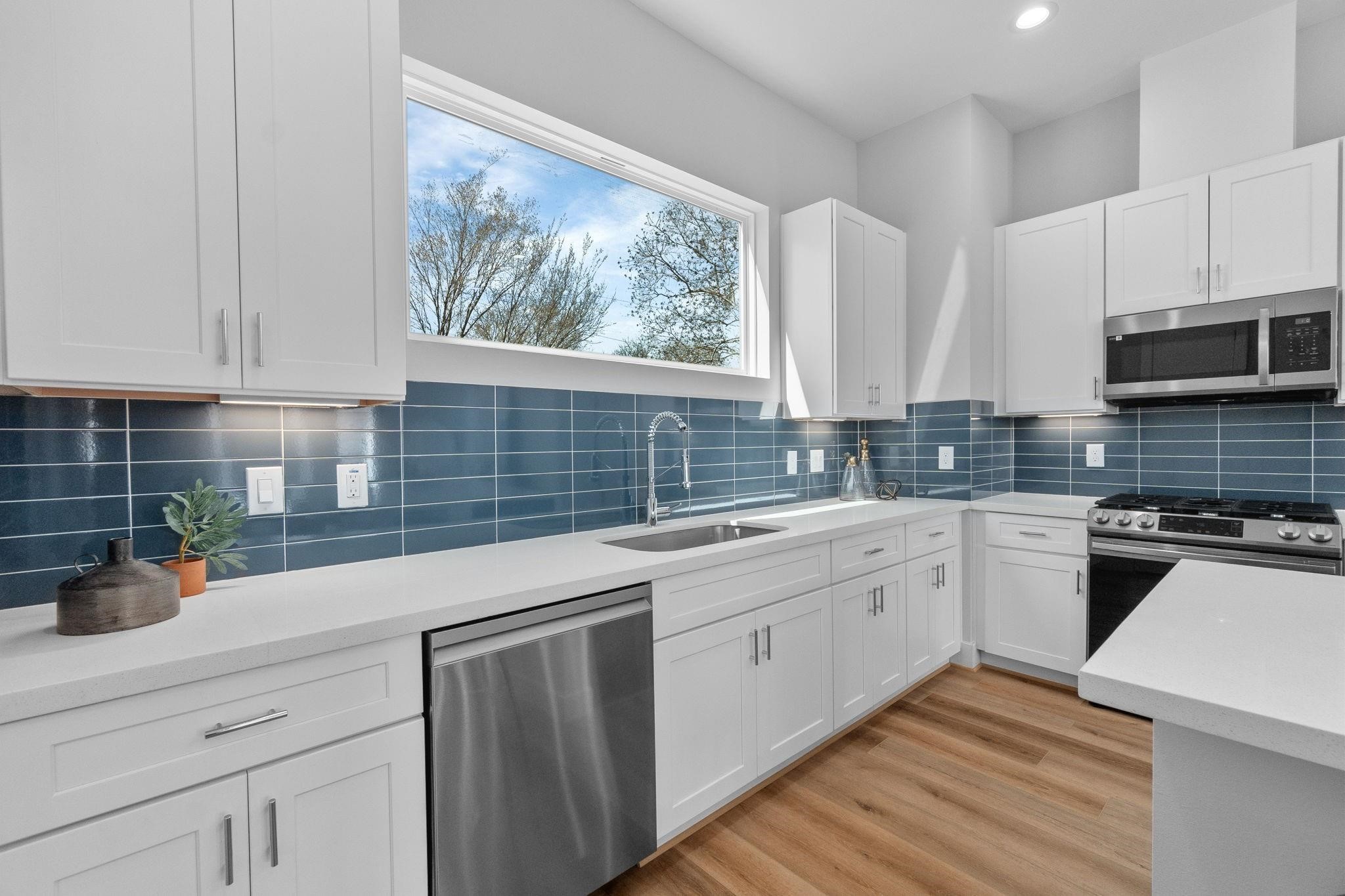 903 Quitman Street, Unit B Houston, TX 77009 - Photo 7 of 23 Designer kitchen featuring quartz countertops, shaker-style cabinetry, stainless steel appliances, and a sleek tile backsplash, all anchored by a large picture window for natural light.
