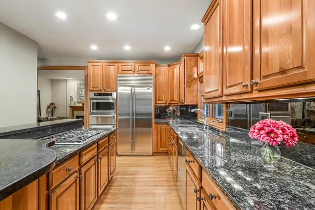 a large living room with stainless steel appliances kitchen island granite countertop a refrigerator a stove a sink dishwasher with a dining table and chairs with wooden floor