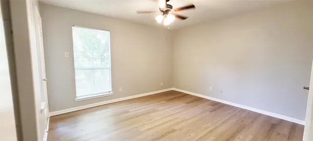 an empty room with wooden floor fan and windows