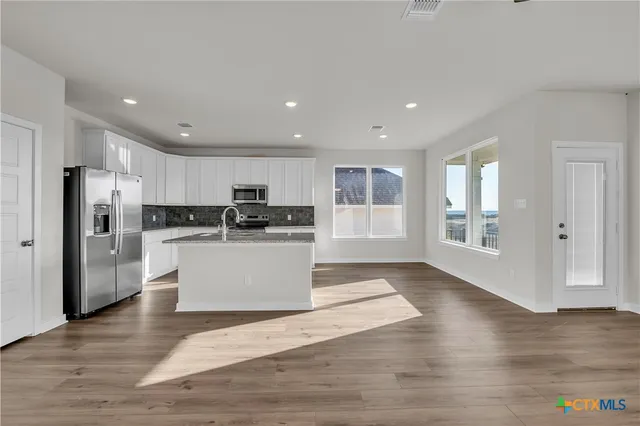 a view of kitchen with granite countertop refrigerator and white cabinets