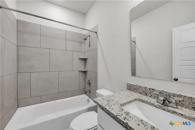 a bathroom with a granite countertop bathtub sink vanity mirror and toilet