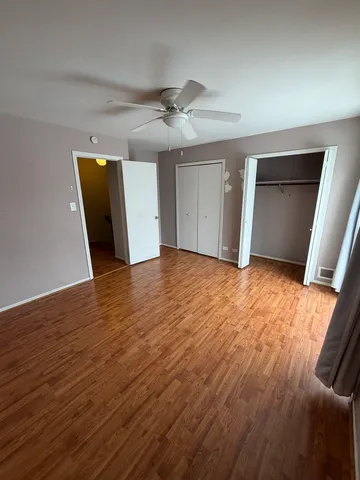 a view of an empty room with wooden floor and a ceiling fan