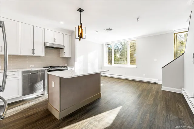 a kitchen with stainless steel appliances a stove a sink and white cabinets with wooden floor next to windows