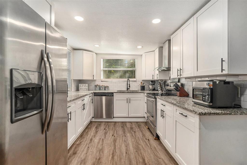 4921 6th Street Zephyrhills, FL 33542 - Photo 3 of 15 a kitchen with granite countertop a refrigerator oven a sink dishwasher and white cabinets with wooden floor