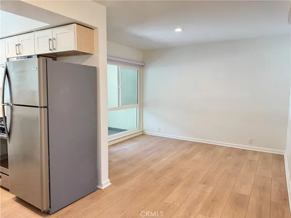 a view of a refrigerator in kitchen and an empty room with wooden floor