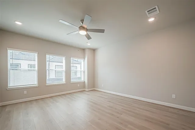 an empty room with wooden floor fan and windows