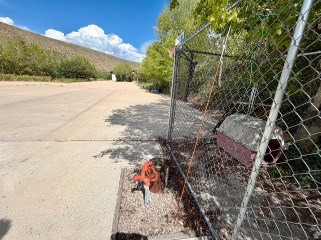 1133 Paris Canyon Road Paris, ID 83261 - Photo 62 of 75 Paved concrete driveway with a rustic-style water pump, set against a backdrop of natural landscaping and a chain-link dog enclosure