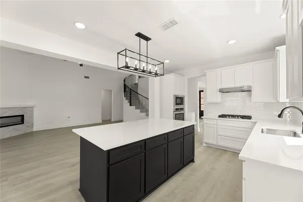 a kitchen with kitchen island white cabinets a sink dishwasher and a stove with wooden floor