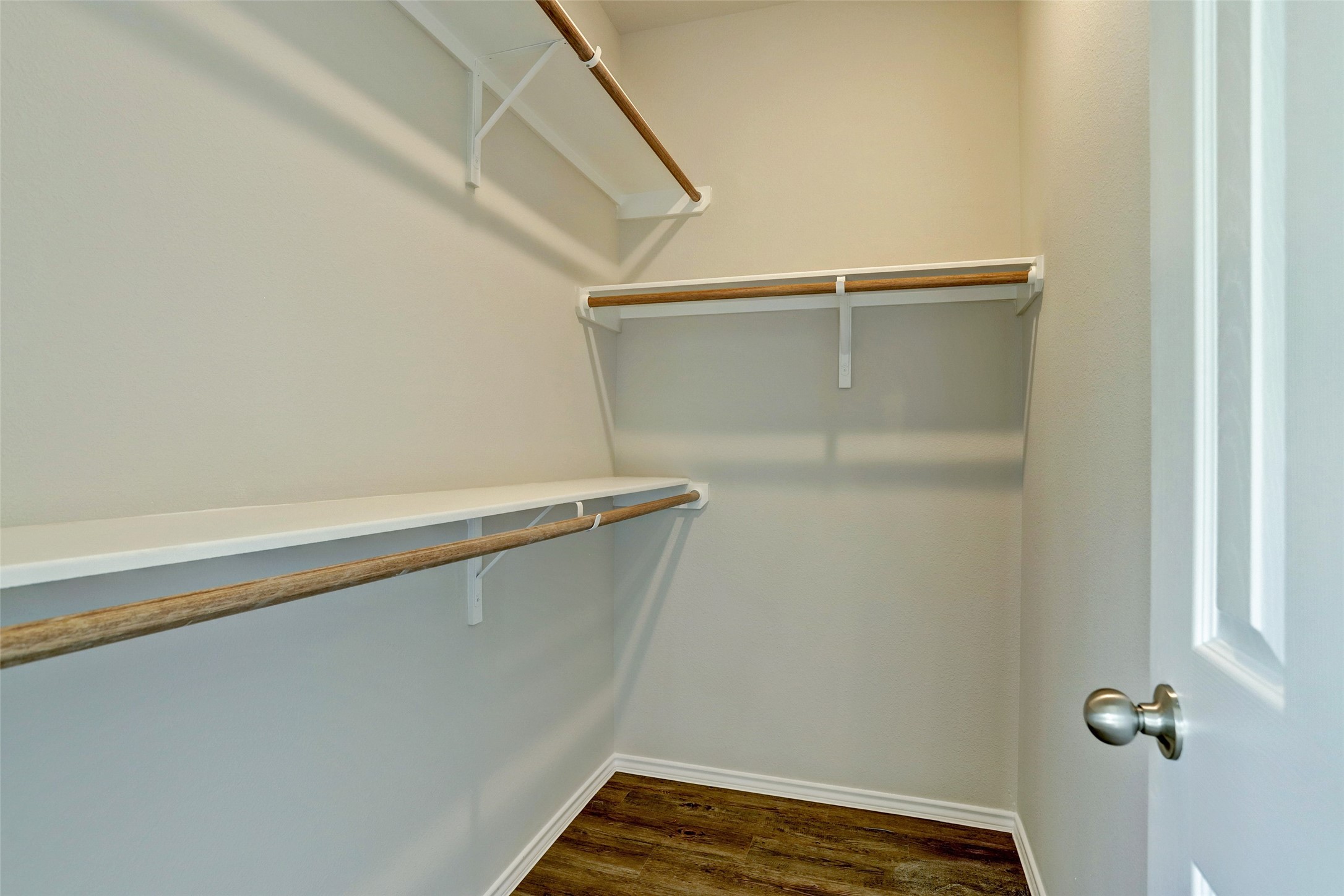 409 South 12th Street, Unit B Conroe, TX 77301 - Photo 12 of 14 This photo shows a spacious walk-in closet with wooden shelves and rods for hanging clothes. The closet features a clean, neutral color palette with a hardwood floor, providing ample storage space.