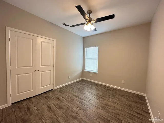 an empty room with wooden floor closet and windows