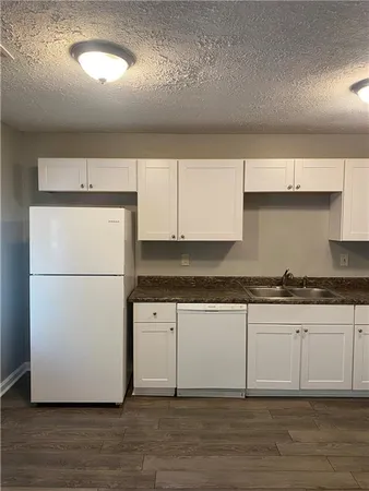a kitchen with granite countertop a stove a refrigerator and a sink with wooden floors