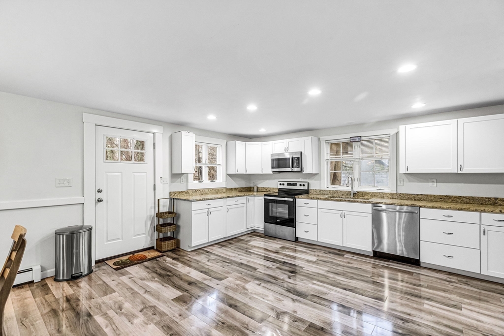 63 South Cottage Road Holland, MA 01521 - Photo 7 of 35 a large white kitchen with granite countertop a stove a sink a refrigerator and white cabinets with wooden floor