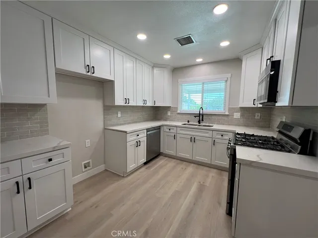 a kitchen with granite countertop white cabinets stainless steel appliances a sink and a window