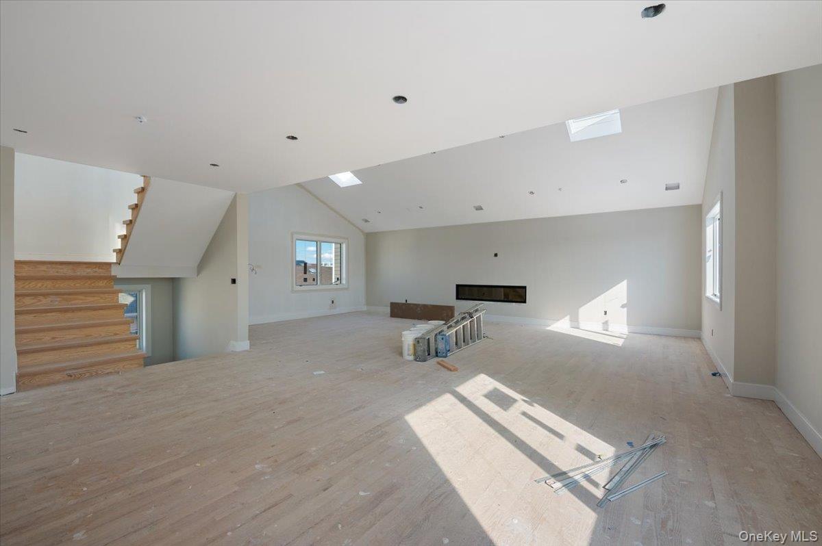 56 Oregon Street Long Beach, NY 11561 - Photo 2 of 25 Unfurnished living room with lofted ceiling, a glass covered fireplace, stairs, wood finished floors, and a skylight