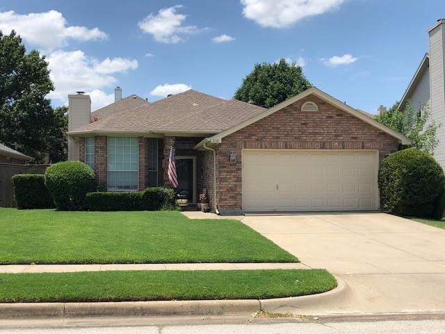 Ranch-style house featuring brick siding, an attached garage, concrete driveway, roof with shingles, and a front yard