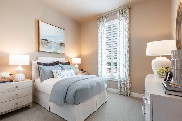 a bedroom with a bed and a lamp on dresser next to a window