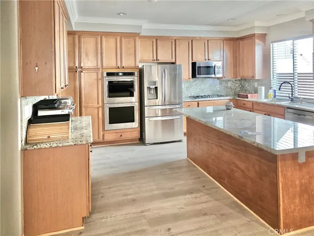 a kitchen with stainless steel appliances granite countertop a refrigerator a stove and a sink with wooden cabinets