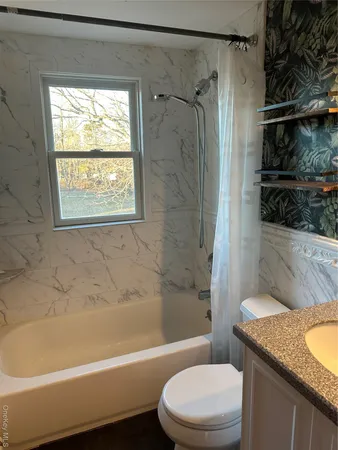 a bathroom with a granite countertop bathtub shower sink vanity and toilet
