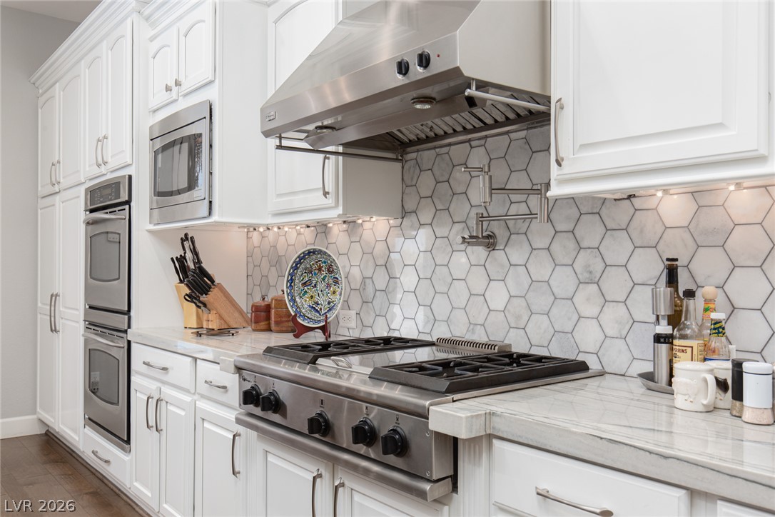 22 Douglas Grove Road Henderson, NV 89052 - Photo 30 of 72 White cabinetry, stainless steel appliances, and hexagon tile backsplash define this well-appointed kitchen.