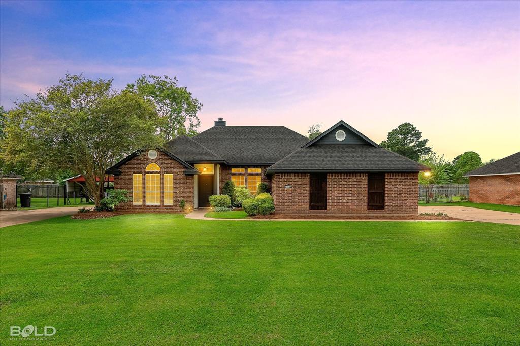 The property features a brick exterior, a dark shingle roof, and an expansive front lawn