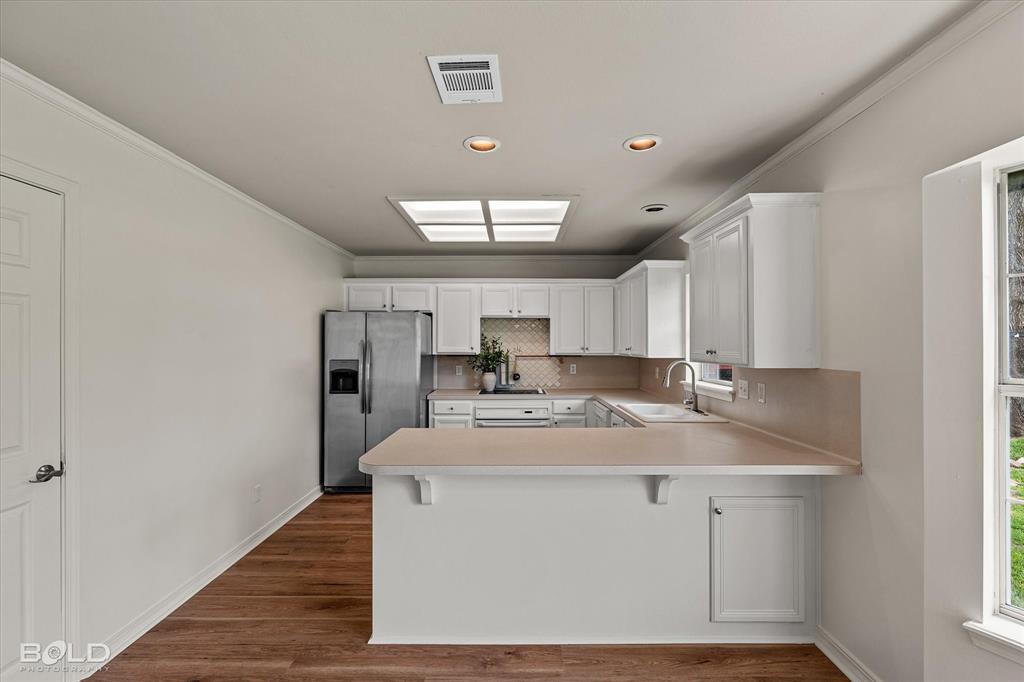 1962 Palmetto Road Benton, LA 71006 - Photo 11 of 40 The kitchen features white cabinetry, a stainless steel refrigerator, and a breakfast bar with a light-colored countertop