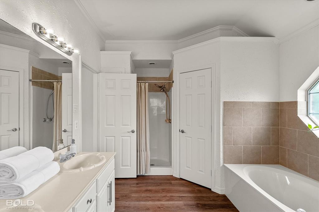 1962 Palmetto Road Benton, LA 71006 - Photo 18 of 40 The bathroom features a double vanity with a large mirror and overhead lighting, a shower with a curtain, and a bathtub with tiled surround