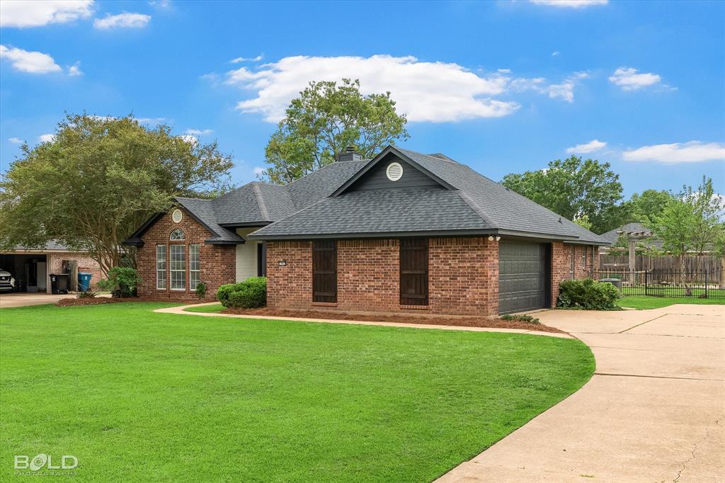 1962 Palmetto Road Benton, LA 71006 - Photo 34 of 40 The property features an extensive green lawn, a brick exterior, a dark shingle roof, and a paved driveway leading to an attached garage